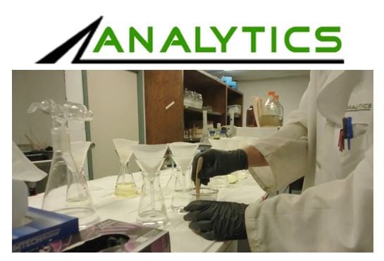 Analytics Corporation employee in lab coat with gloves on stirring liquid in beaker